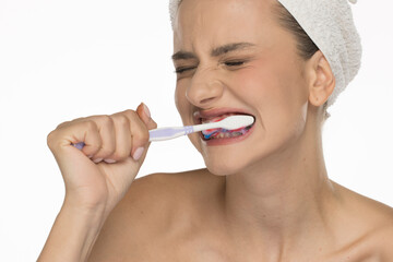 Young woman brushing her teeth with expression of effort, studio shot on white background.
