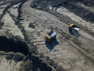 Heavy quarry dump trucks carry coal in their backs.