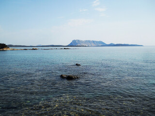 Breathtaking sea view featuring the majestic Tavolara Island off the coast of Sardinia, Italy. The crystal-clear turquoise waters of the Mediterranean Sea stretch toward the horizon, with the dramatic