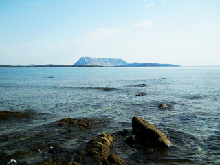 Beautiful sea view featuring the majestic Tavolara Island off the coast of Sardinia, Italy. The crystal-clear turquoise waters of the Mediterranean Sea stretch toward the horizon, with the dramatic