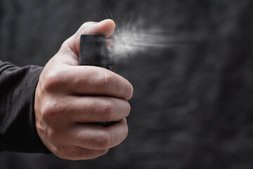 Close-up of a man hand pressing a pepper spray canister with visible aerosol release. Concept self-defense, protection, danger prevention, and personal safety.