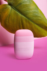 Minimalist pink silicone facial cleansing device on vibrant pastel background, modern skincare and beauty technology tool for gentle hygiene and self-care routine