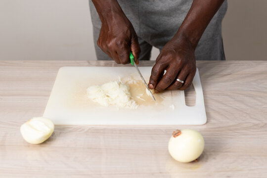 Black male hands chopping fresh onion on chopping board