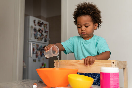 Focused toddler boy playing with bowls and water at home