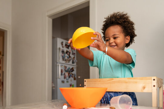 Smiling toddler boy playing with bowls and water at home