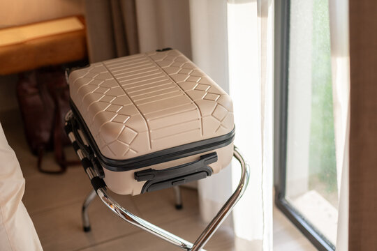 Beige carry-on suitcase on luggage rack in hotel room, close up
