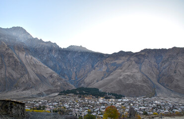 Vast Caucasus mountain range looms over a village of Stepantsminda nestled in a valley, with sparse...