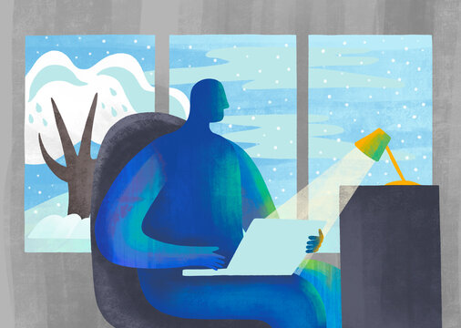 Individual working on a laptop by a large window with winter view