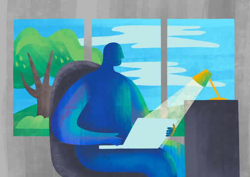 Individual working on a laptop by a large window with summer view