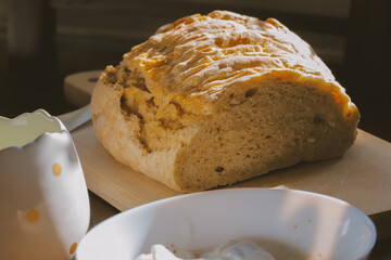 Rustic homemade bread loaf on wooden cutting board in natural sunlight, traditional artisan baking with golden crust and soft interior, comfort food concept