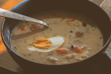 Traditional Polish sour rye soup (żurek) served with boiled egg and vegetables in a rustic black bowl, classic Easter dish from Eastern European cuisine