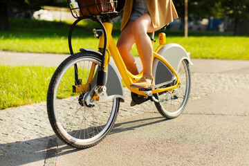 Cropped shot of young woman cycling in the park, riding electric bicycle, closeup of female legs