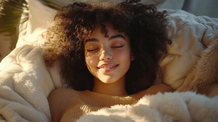 Young woman with curly hair peacefully relaxing and smiling with closed eyes wrapped in a soft blanket in warm light