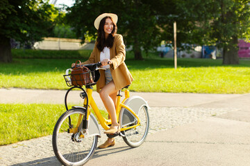 Young European lady in summer outfit riding rental electric bike in the summer in the city park,...