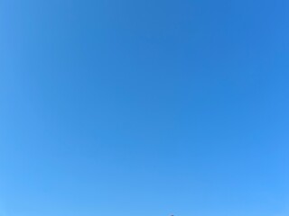 Clear blue sky with a small part of a house roof at the bottom. Minimal composition, ideal for design, background use, real estate, architecture, and outdoor atmosphere concepts.