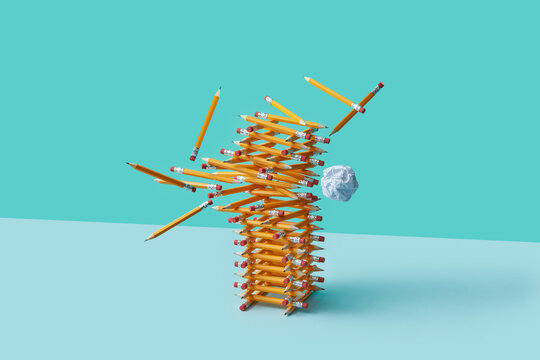 Falling pencil tower hit by paper on blue background