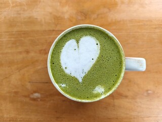 Close-up of a matcha green tea latte with heart-shaped foam art on a wooden table. A cozy and...