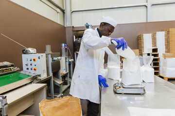 Worker adding glucose to plastic bag on scale during packaging process
