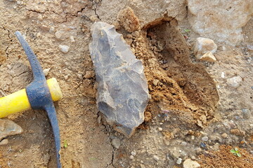 Stone similar to a large flint axe found in the sand lies next to a pickaxe, field photo at a quarry