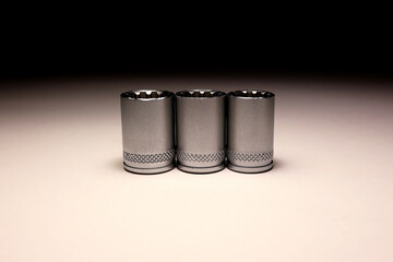 Three metal socket wrench bits in a row on light background, minimalist industrial tool...