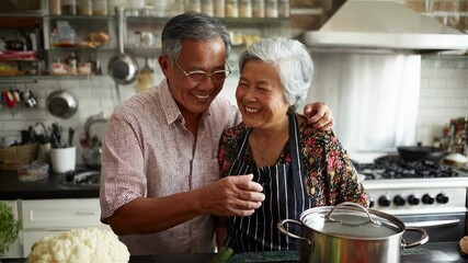 A cheerful senior Asian couple shares a lighthearted moment in their kitchen embracing each other during a cooking break. With colorful ingredients spread across the counter and a pot - Powered by Adobe