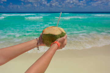 Coconut with a straw in female hands on the background of the sea