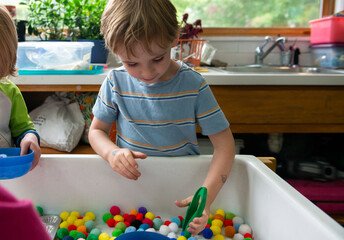Child works gross motor skills, using tweezers at sensory table