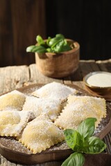 Uncooked ravioli and basil on wooden table, closeup