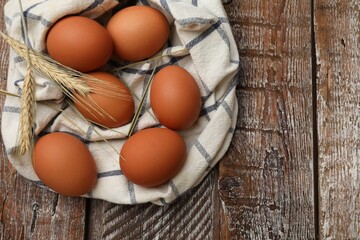Raw eggs, fabric and spikes of wheat on wooden table, top view. Space for text