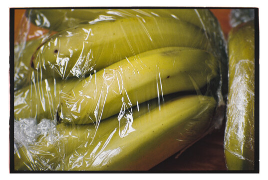 Fresh bananas wrapped in plastic on a wooden surface