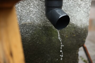 Water dripping from drain pipe outdoors, closeup