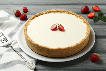 One tasty cheesecake, strawberries and server on grey wooden table, closeup