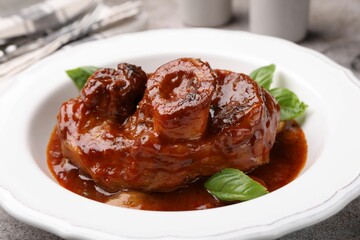 Traditional ossobuco dish with beef steak, sauce and basil on table, closeup