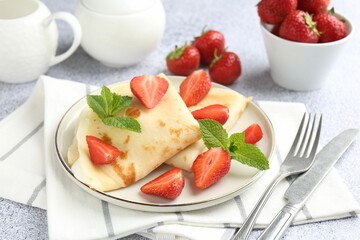 Tasty crepes with cream, strawberries and mint served on light gray table, closeup