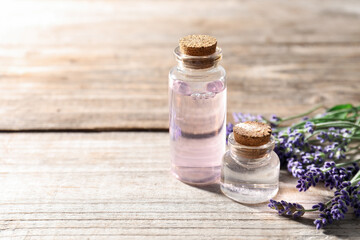 Natural essential oil and lavender flowers on wooden table, closeup. Space for text