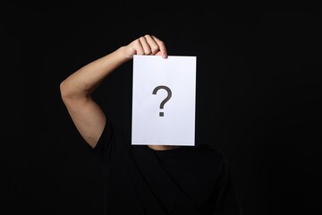 Man hiding behind paper sheet with question mark on dark background