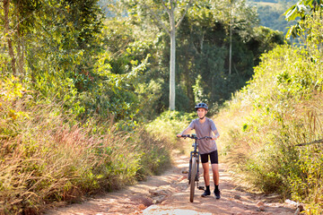 Obraz premium Cyclist walking his mountain bike up a trail surrounded by nature. Promoting well-being, fitness, and outdoor adventure