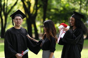 Three graduates pose happily in caps and gowns, holding diplomas and a bouquet, celebrating their...