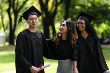 Three graduates pose happily in caps and gowns, holding diplomas and a bouquet, celebrating their...