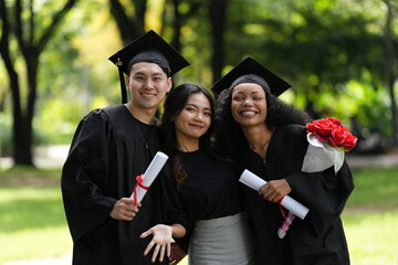 Three graduates pose happily in caps and gowns, holding diplomas and a bouquet, celebrating their...