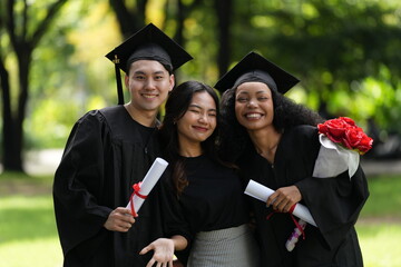 Three graduates pose happily in caps and gowns, holding diplomas and a bouquet, celebrating their...