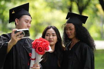 Three graduates pose happily in caps and gowns, holding diplomas and a bouquet, celebrating their...