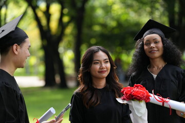 Three graduates pose happily in caps and gowns, holding diplomas and a bouquet, celebrating their...