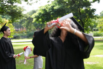 A graduate in cap and gown gazes upward with a joyful smile, holding her diploma. Behind her, two...
