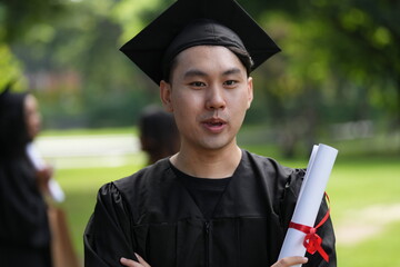 A joyful graduate in a black cap and gown proudly raises his diploma with excitement, looking...