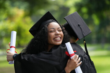 Two graduates in gowns share a warm embrace, holding diplomas with smiles of joy and pride. The...