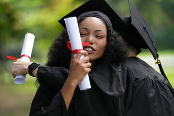 Two graduates in caps and gowns joyfully celebrate, each holding a diploma with smiles and raised...
