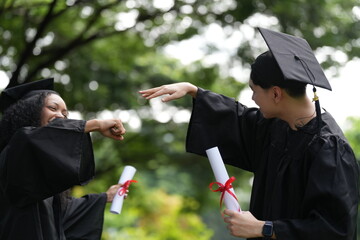 Two graduates in caps and gowns joyfully celebrate, each holding a diploma with smiles and raised...