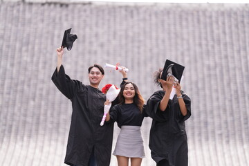 Three graduates celebrate with raised caps and diplomas, smiling joyfully. The two in gowns stand...