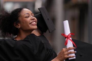 Two graduates in caps and gowns beam with joy, embracing and cheering in celebration. Their wide...